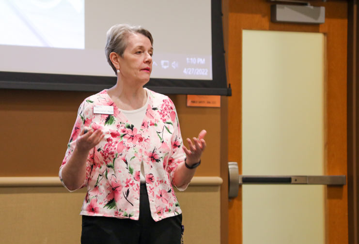 woman in floral shirt presenting at a conference