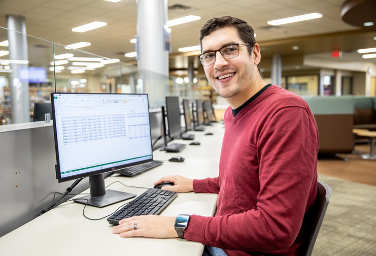 Man with red shirt in computer lab with Excel document open