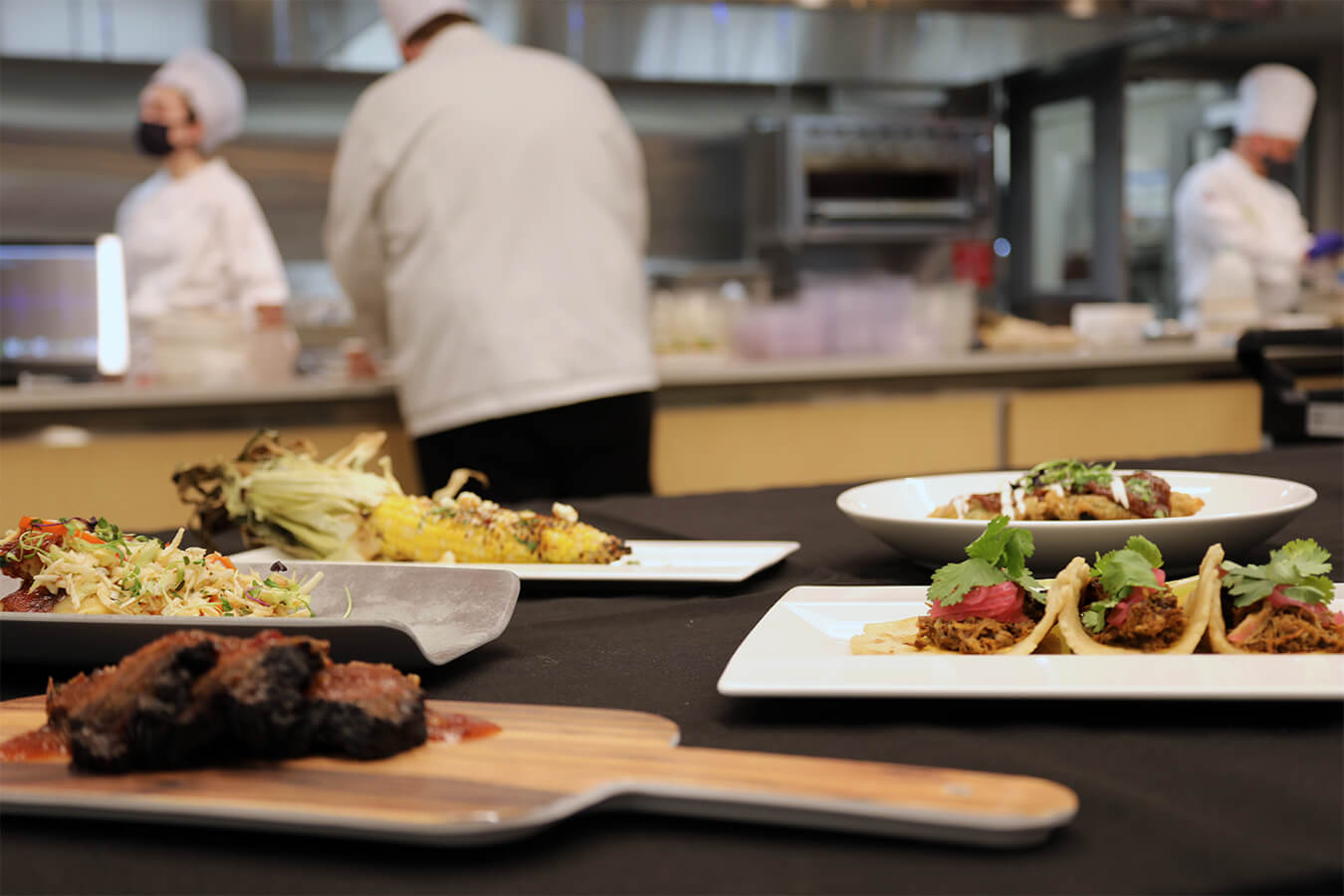 Assorted plated menu items with chefs in background