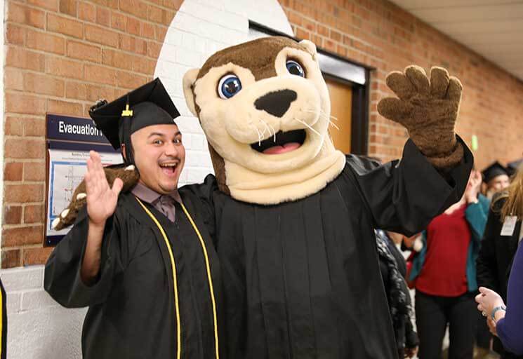 CVTC graduate and Ollie Otter standing together smiling and waving