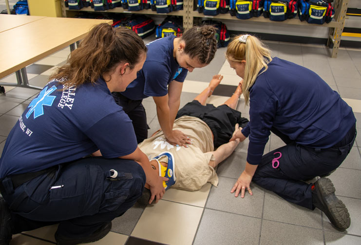 Paramedic students training around a medical manikin