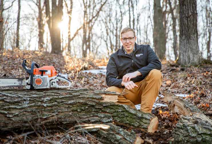 Man in woods with chainsaw and tree trunk.