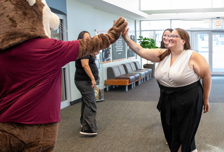 Woman in a college building high-fiving a college mascot