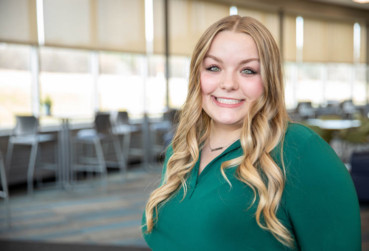 Blonde girl in green shirt posing in a college commons