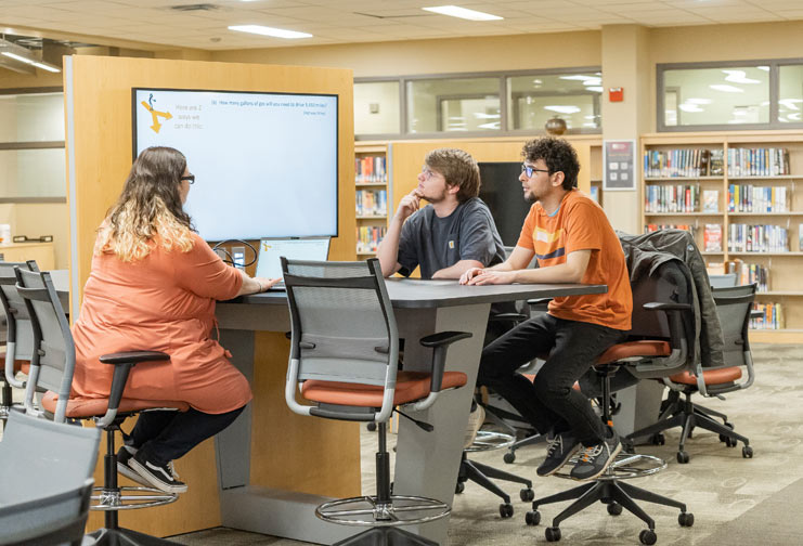 Two male and one female student use the library at college to work on a project