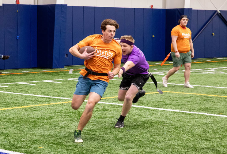 Man in flag football league runs with the football as another man reaches for his flag to stop the play.