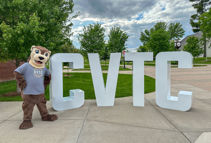 Ollie the CVTC River Otter in a CVTC T-shirt standing in front of the CVTC letters