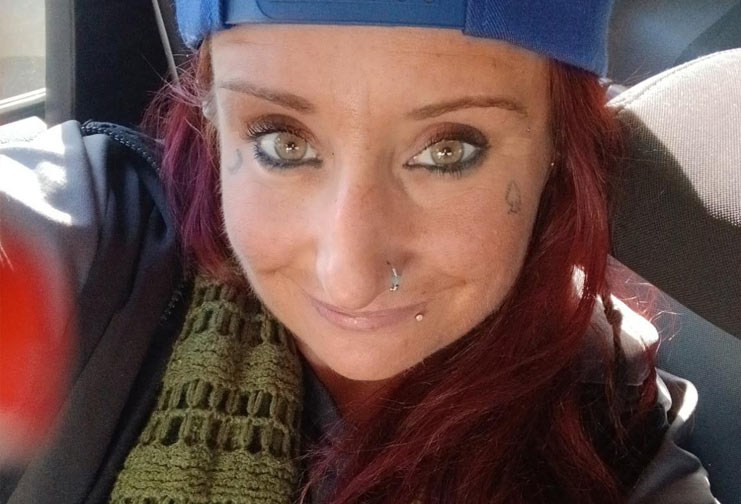 Woman in backwards baseball cap and scarf taking selfie photo in a vehicle.